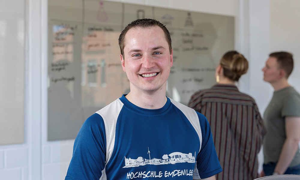 Portrait eines jungen Mannes. Der Mann hat sehr kurze Haare, trägt ein Sporttrikot mit dem Namen der Hochschule Emden/Leer und lächelt in die Kamera.